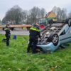 Auto belandt op kop naast rotonde